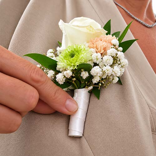 Boutonnière fleurie assortie au bouquet de mariée, composée de fleurs blanches et pastel pour un mariage à Hyères